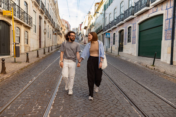 Улыбающаяся влюбленная пара, держащаяся за руки во время прогулки по старой городской улице. Высокое качество фото - Фото, изображение