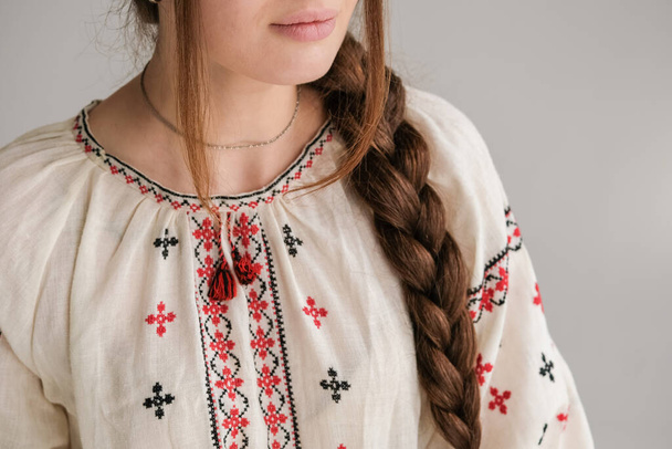 Großaufnahme eines traditionell bestickten ukrainischen Hemdes Vyshyvanka auf einem Mädchen mit geflochtenem Haar. Ukrainisches Mädchen im traditionellen Hemd namens Vyshyvanka. Ukrainische Vyshyvankas zeichnen sich durch stickspezifische Merkmale der ukrainischen Stickerei aus. - Foto, Bild