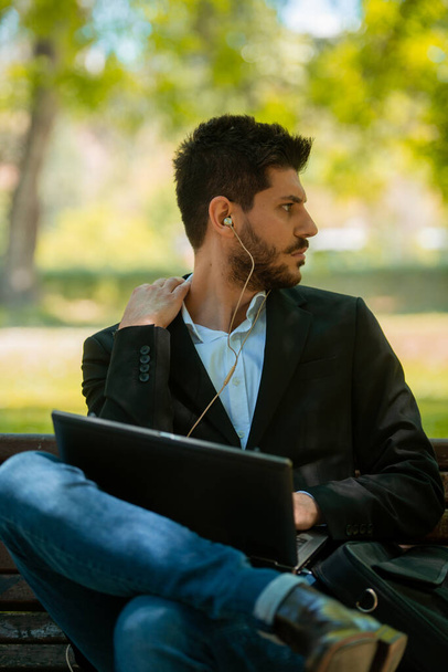 Homme d'affaires assis sur le banc avec son ordinateur portable et écouteurs - Photo, image
