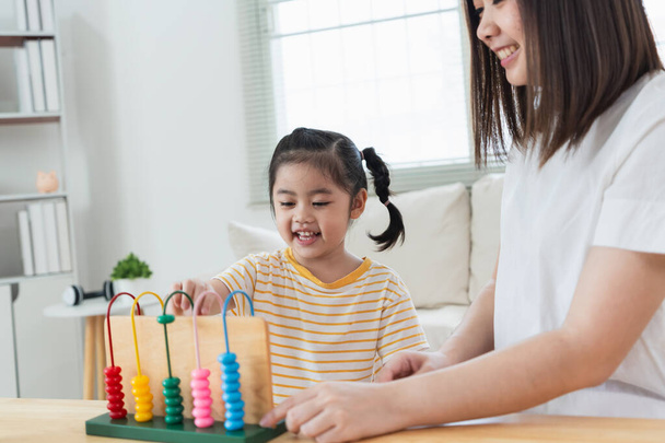 jong schattig aziatisch meisje en haar ouder moeder moeder is het leren van de abacus met gekleurde kralen om te leren hoe om te tellen bank in de woonkamer thuis. Kind baby meisje ontwikkeling studing concept. - Foto, afbeelding
