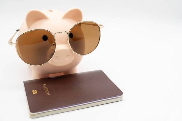 Hucha con gafas de sol y pasaporte preparándose para las vacaciones. Ahorro de dinero, concepto de viaje. Fondo aislado. - Foto, Imagen
