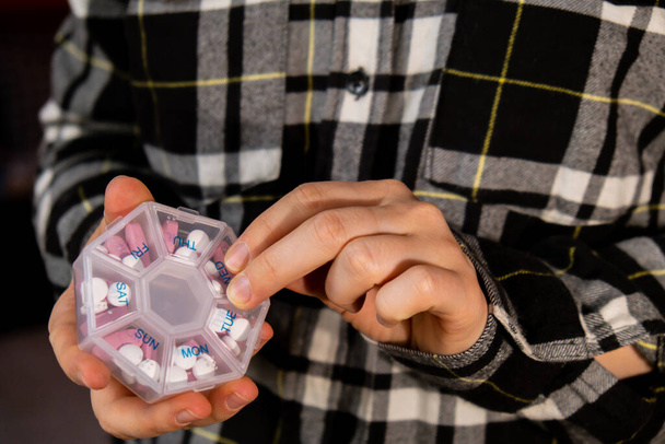 Ženské ruce třídění pilulky Organizátor týdenní záběry Detailní záběr lékařské pilulky box s dávkami tablet pro denní užívat léky s bíle růžové léky a kapsle. Mladá žena dostává své denní vitamíny - Fotografie, Obrázek