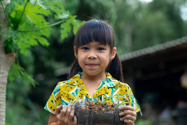 Meisje toont jonge boompjes gekweekt in gerecycleerde plastic flessen. Recycle waterfles pot, tuinieren activiteiten voor kinderen. Recycling van kunststofafval - Foto, afbeelding