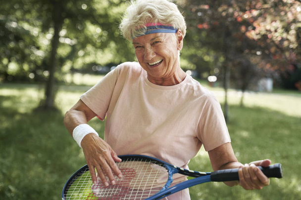 Retrato de una mujer mayor parada en el parque y sosteniendo raqueta de tenis - Foto, Imagen