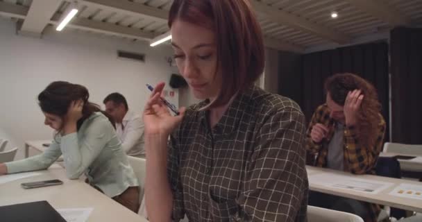 Όμορφη νεαρή γυναίκα δίνει εξετάσεις που περιβάλλονται από άλλους μαθητές στην τάξη - Πλάνα, βίντεο