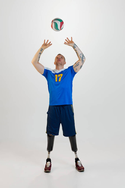 Un joven atractivo con discapacidad protésica en la pierna de pie lanza una pelota de voleibol. Deporte inclusivo para personas con discapacidad. concepto de deporte, jugador, médico, salud, cuidado del cuerpo. - Foto, Imagen