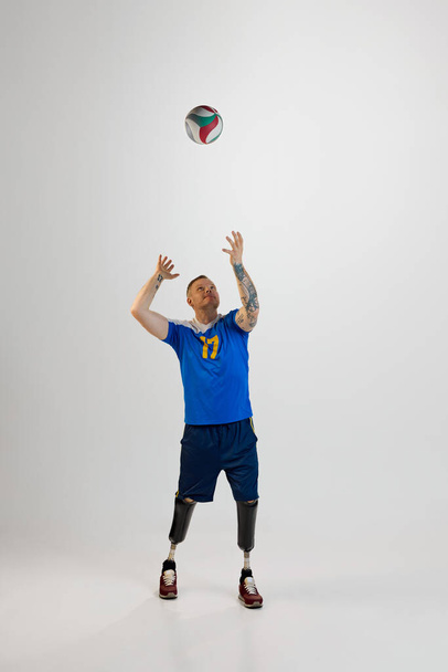 Atrakcyjny młodzieniec z protezą nogi stojący przy piłce do siatkówki. Sport integracyjny dla osób niepełnosprawnych. koncepcja sportu, zawodnika, medycyny, zdrowia, pielęgnacji ciała. - Zdjęcie, obraz