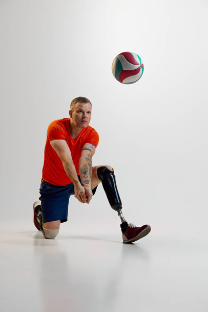 Hombre seguro con piernas protésicas, discapacidad en uniforme golpea pelota de voleibol en movimiento en el suelo. Deporte inclusivo para personas con discapacidad. concepto de deporte, jugador, médico, salud, cuidado del cuerpo. - Foto, imagen