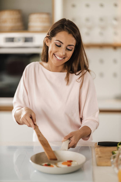 Kuvattu nuori nainen valmistelee paistettuja munia aamiaiseksi keittiössään. - Valokuva, kuva