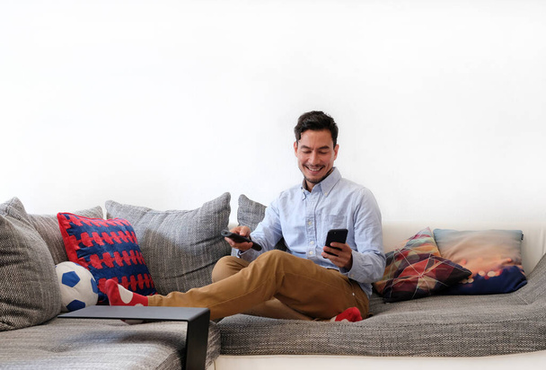 Second screen - smiling man with remote control and smartphone - Photo, Image