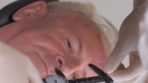 Orvossebész portréja, amint sebeket hagy a férfi arcán, idős férfi. Függőleges videó. - Felvétel, videó