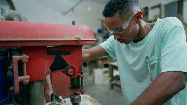 Um jovem aprendiz de carpintaria preta feliz usando máquina industrial, vira-se para a câmera sorrindo. Retrato amigável de um trabalhador envolvido com a ocupação do trabalho - Foto, Imagem