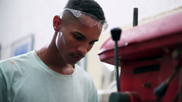 Un joven trabajador brasileño negro utilizando la máquina de perforación para agujero masculino en la superficie de madera en el taller de carpintería - Foto, imagen