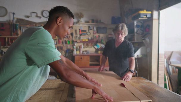 Cena da oficina de marcenaria de Master Carpenter e jovem aprendiz trabalhando na oficina de carpintaria cortando pedaço de madeira com máquina de serra - Foto, Imagem