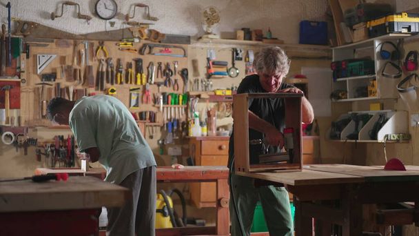 Scena artigianale di lavorazione del legno di falegnami. Laboratorio di falegnameria con occupazione di anziano e apprendista - Foto, immagini