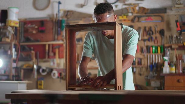 Engaged in Craft scene of a Young Black Brazilian Carpenter Building Furniture at Workshop, apprentice using drilling equipment, wood carpentry student - Фото, изображение