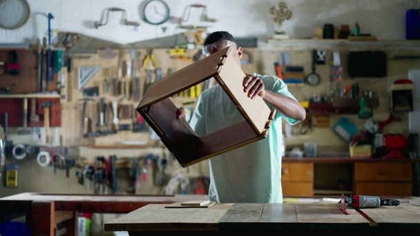 Un joven carpintero brasileño negro se dedica a la artesanía de muebles de construcción de trabajo en el taller - Foto, Imagen