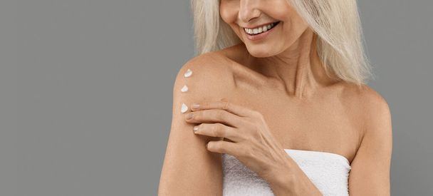 Anti-Aging Skincare. Smiling Mature Woman Applying Body Lotion On Shoulder, Unrecognizable Older Lady Moisturising Skin, Using Nourishing Cream While Standing Isolated On Grey Background, Copy Space - Foto, afbeelding