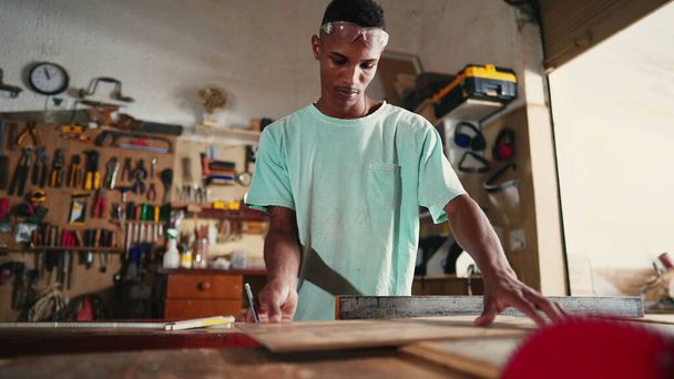 Skoncentrowany młody brazylijski stolarz Learning Profession w Warsztacie, przy użyciu piły do cięcia drewna - Zdjęcie, obraz