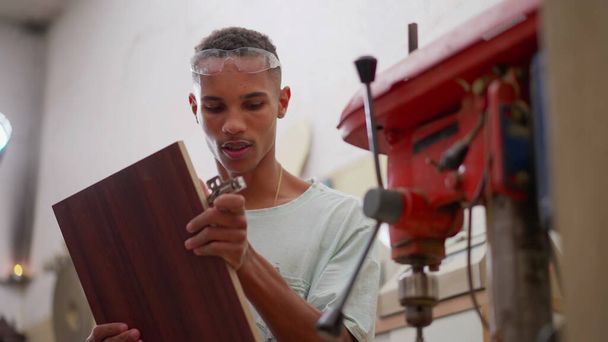 Jeden brazylijski czarny młody cieśla pracujący w stolarni stolarskiej obok maszyny przemysłowej, zawód ucznia zajmującego się pracą - Zdjęcie, obraz