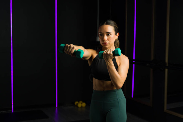 Mulher jovem mexicana em um centro de fitness high-end trabalhando fora usando pesos haltere e fazendo treinamento funcional - Foto, Imagem