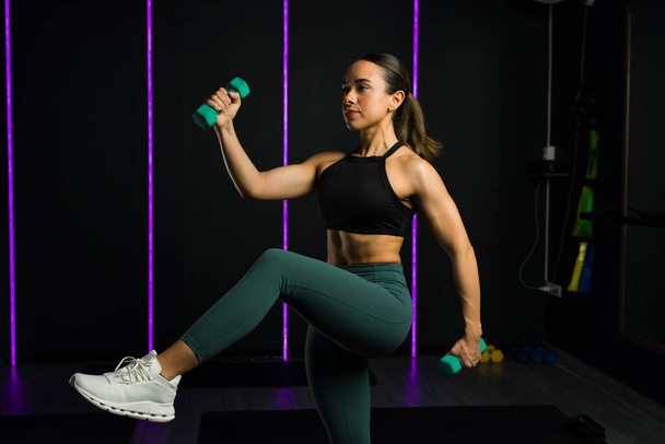 Активна латиноамериканська жінка робить високоінтенсивний інтервал тренування або кардіо-гіт-тренування з використанням гантелі ваги в спортзалі - Фото, зображення