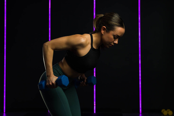 Giovane donna latina attiva al centro fitness che si allena con i pesi dei manubri per un corpo atletico durante l'allenamento incrociato - Foto, immagini
