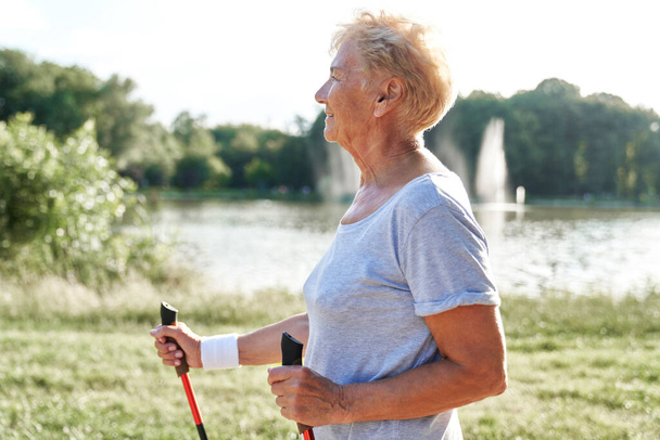 Seitenansicht einer Seniorin beim Nordic Walking im Park - Foto, Bild