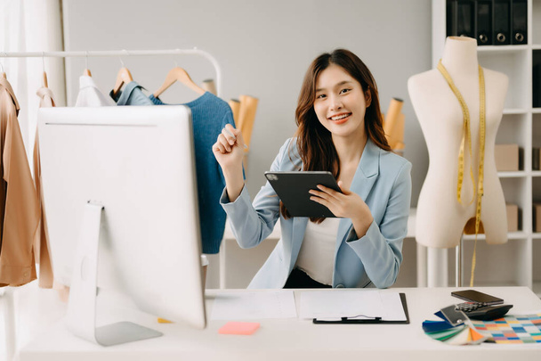 Successful fashion designer. Attractive young asian woman working in studio as dressmaker - 写真・画像
