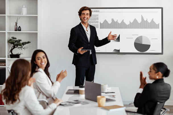 ビジネスマンとビジネスススピーカーとのビジネスミーティングは,多種多様な同僚にマーケティング統計を提供し,スクリーンとチームサポートの統計で成功と拍手を発表します - 写真・画像