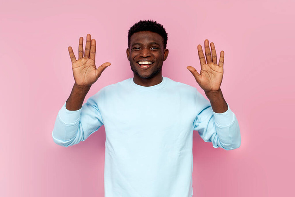 Παραιτούμαι. Αφροαμερικάνος με μπλε πουλόβερ σηκώνει τα χέρια του σε ροζ απομονωμένο φόντο, ο άνθρωπος δείχνει άδειες παλάμες και χαμόγελα. - Φωτογραφία, εικόνα