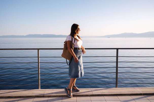Привлекательная женщина в джинсовом стиле стоит перед морским пейзажем. Счастливая женщина смотрит на закат. Высокое качество фото - Фото, изображение