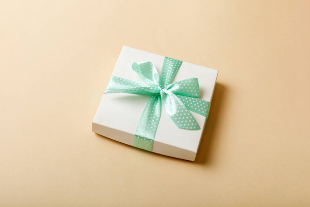 csomagolva karácsony vagy más ünnep kézzel készített ajándék papír lila szalaggal színes háttér. Jelen doboz, díszítés ajándék színes asztalon, felülnézet másolási hellyel. - Fotó, kép