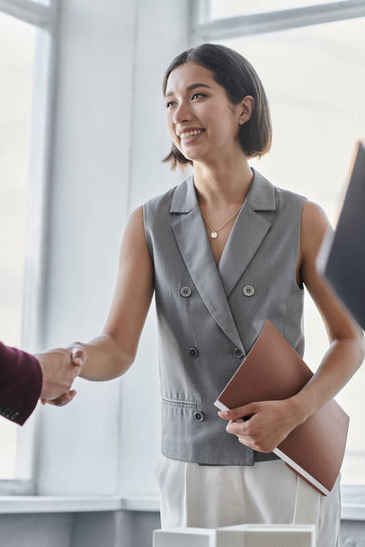 glückliche Geschäftsfrau mit Ordner schüttelt Hände mit Geschäftspartner im Büro, Zusammenarbeit - Foto, Bild