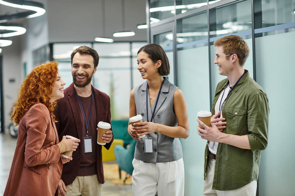 smiling managers holding coffee to go during conversation in modern coworking office - Foto, Imagen