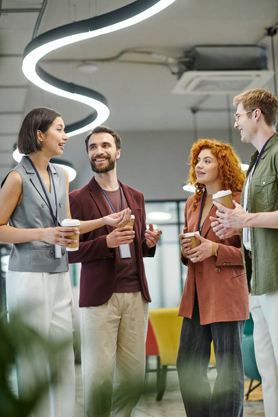 jonge zakenvrouw praten met vrolijke collega 's met papieren bekers, koffiepauze in modern kantoor - Foto, afbeelding