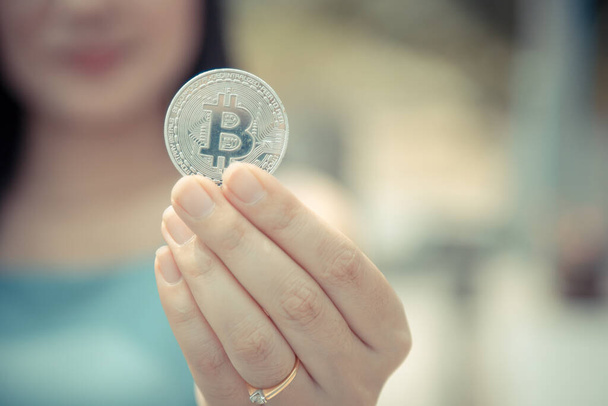 Usmívající se krásná žena drží Bitcoin digitální měny a kryptoměna s rozmazaným pozadím. Koncept bezhotovostní společnosti těžba virtuálních peněz na webu. - Fotografie, Obrázek