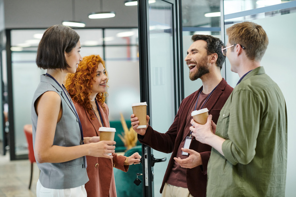 Iloinen parrakas liikemies nauraa kollegoiden lähellä kertakäyttökuppien kanssa, kahvitauko virassa - Valokuva, kuva