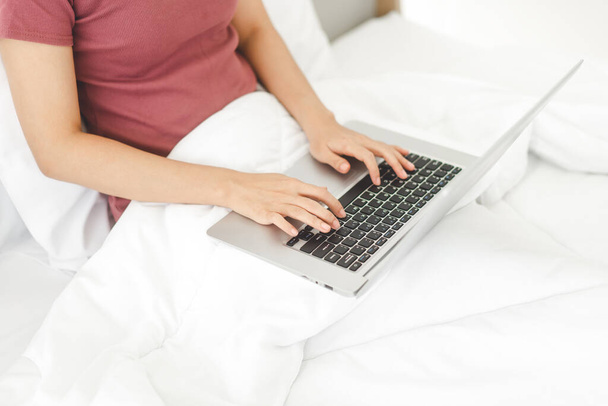 Primeros planos mujer tecleo a mano teclado portátil en la cama. Personas que usan internet para estilos de vida modernos. Fondo con manta blanca - Foto, imagen