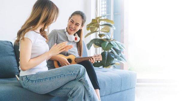 Δύο νέα ενήλικη γυναίκα που ζουν μαζί με την έννοια της σχέσης. Οι Νοτιοασιάτες χαλαρώνουν παίζοντας μουσική στους καναπέδες στο σπίτι. Φόντο μεγέθους banner. - Φωτογραφία, εικόνα