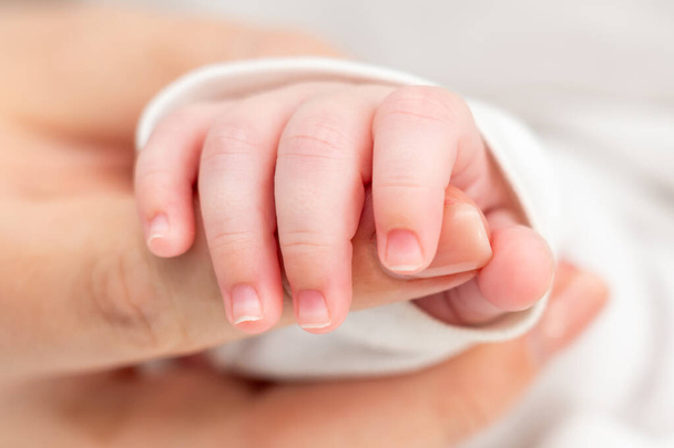 Un neonato, nel sonno profondo, si aggrappa al dito delle madri mostrando pura fiducia e attaccamento. - Foto, immagini