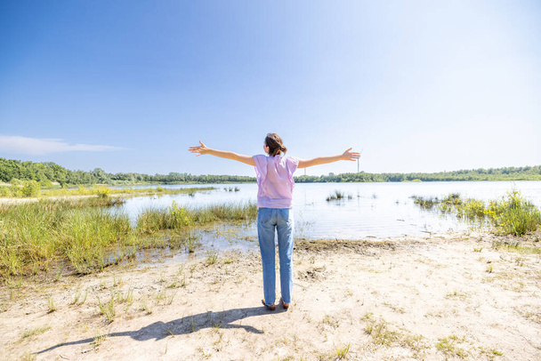 Experience the exuberance of victory and joy in this vibrant image. A happy woman raises her arms in a victory gesture, smiling with the backdrop of lush green trees and natures beauty. Amidst the - Photo, Image
