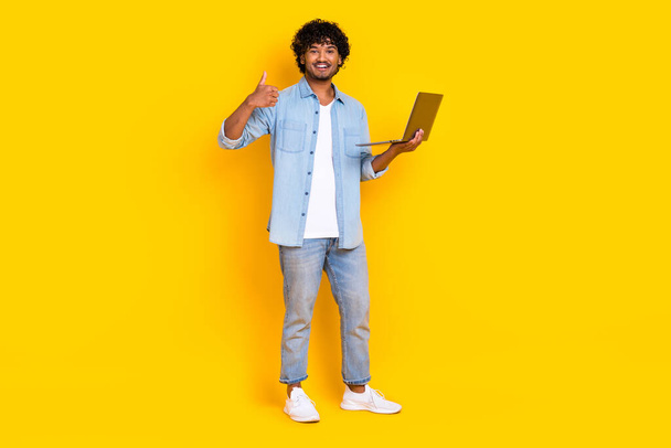 Full size photo of clever man dressed denim shirt stylish jeans hold laptop show thumb up good work isolated on yellow color background. - Фото, зображення