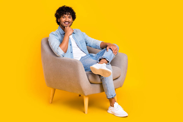 Full size photo of thoughtful smart man dressed denim shirt sit in armchair arm on chin think business isolated on yellow color background. - Zdjęcie, obraz