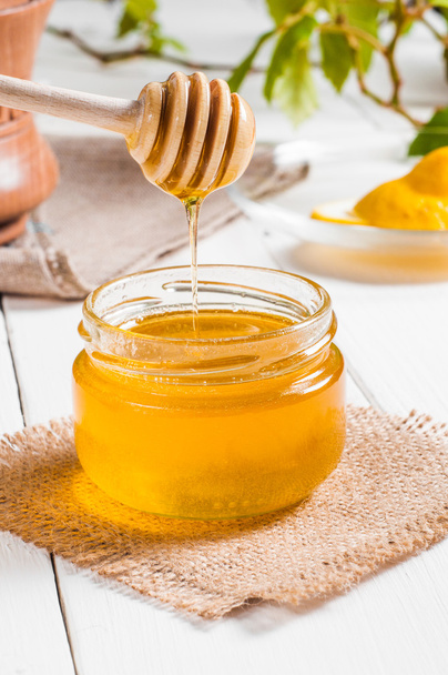 Honey jar with dipper and lemon flowing, wood background - 写真・画像