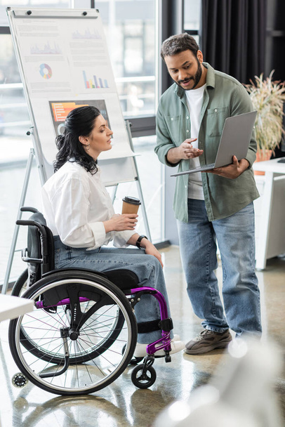 indio hombre mostrando proyecto de inicio en el ordenador portátil a mujer discapacitada en silla de ruedas, concepto de inclusión - Foto, Imagen