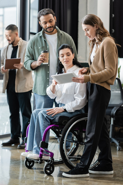 mujer discapacitada en silla de ruedas mirando tableta, discutiendo proyecto de inicio con equipo interracial - Foto, Imagen