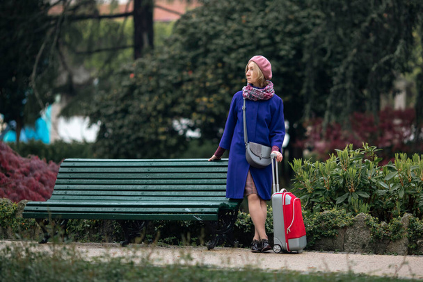 En la plaza hay una mujer con una maleta roja en las manos.. - Foto, Imagen