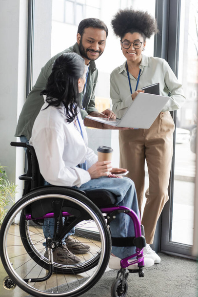 щасливі міжрасові колеги, які дивляться на інвалідів на інвалідному візку, обговорюють стратегію роботи - Фото, зображення