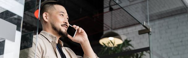 feliz asiático hombre tener negocios llamada telefónica en el teléfono inteligente cerca de la puerta de cristal en la oficina, bandera - Foto, Imagen